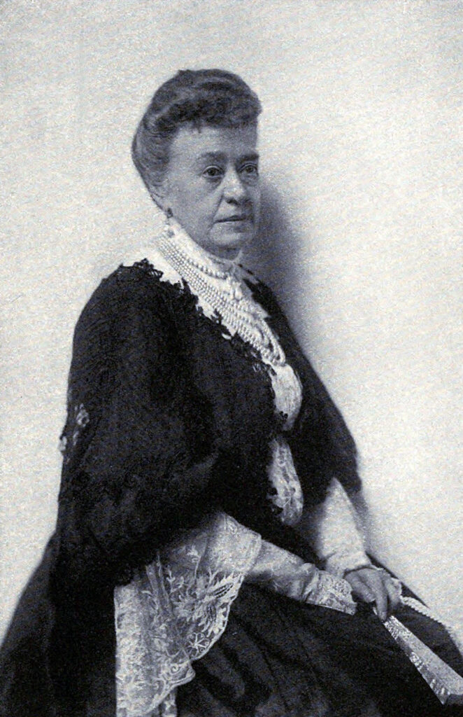 Black and white portrait of Jane Stanford. She is sitting in front of the camera in a black dress with white embroidery. Her look is determined, gazing to the right of the image.